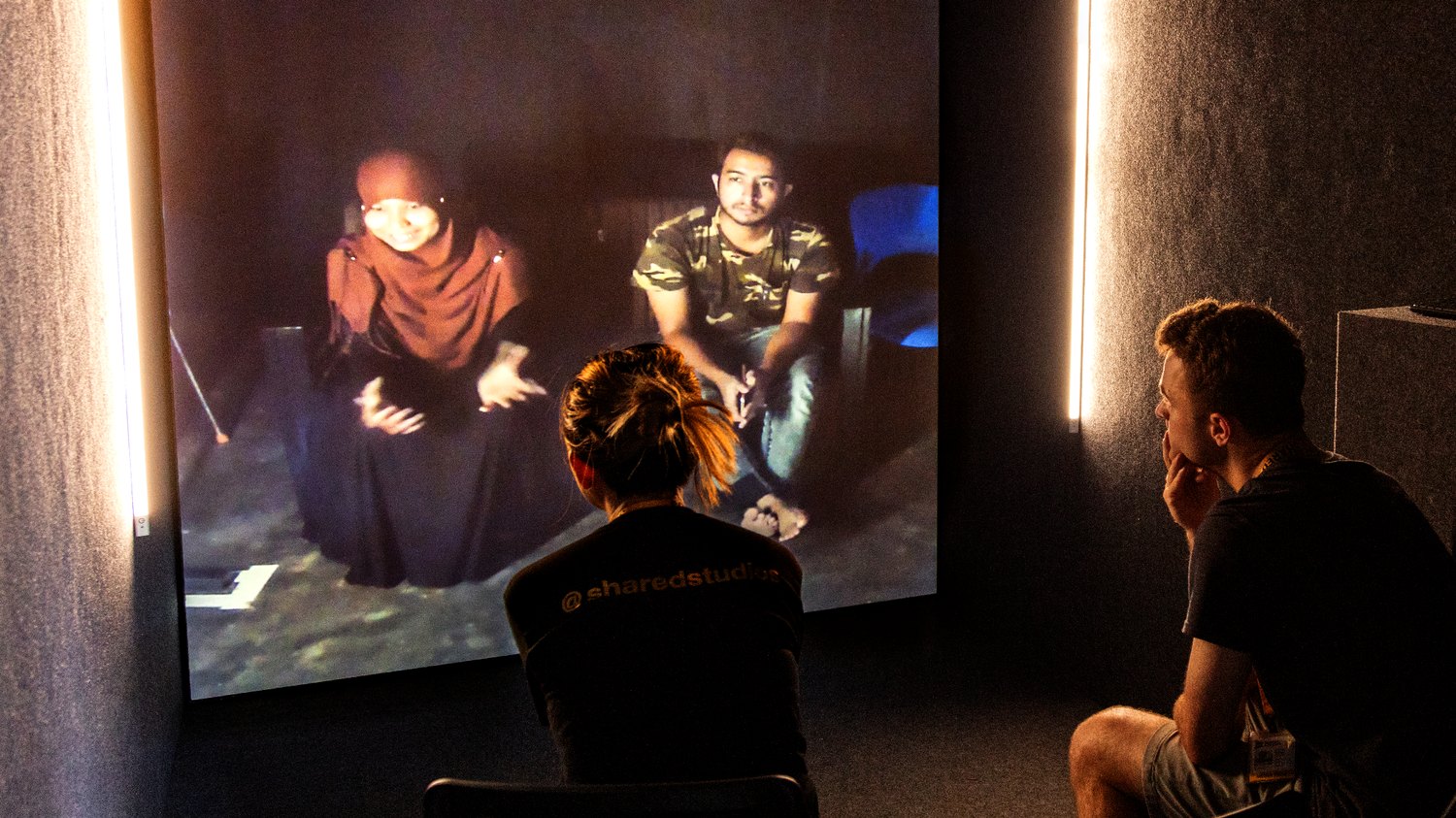 Two visitors in a Portal watching life-size video of a person in Gaza projected on the wall